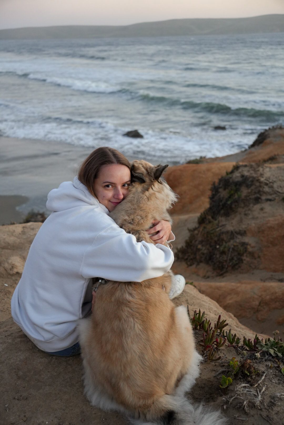 Black-and-white portrait, woman embracing her dog on the cliffs